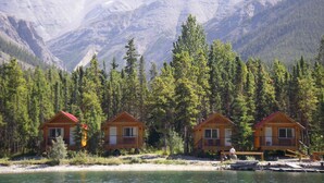 A row of wooden cabins with red roofs, situated by a lake with mountains in the background. - Northern Rockies Lodge (Muncho Lake)