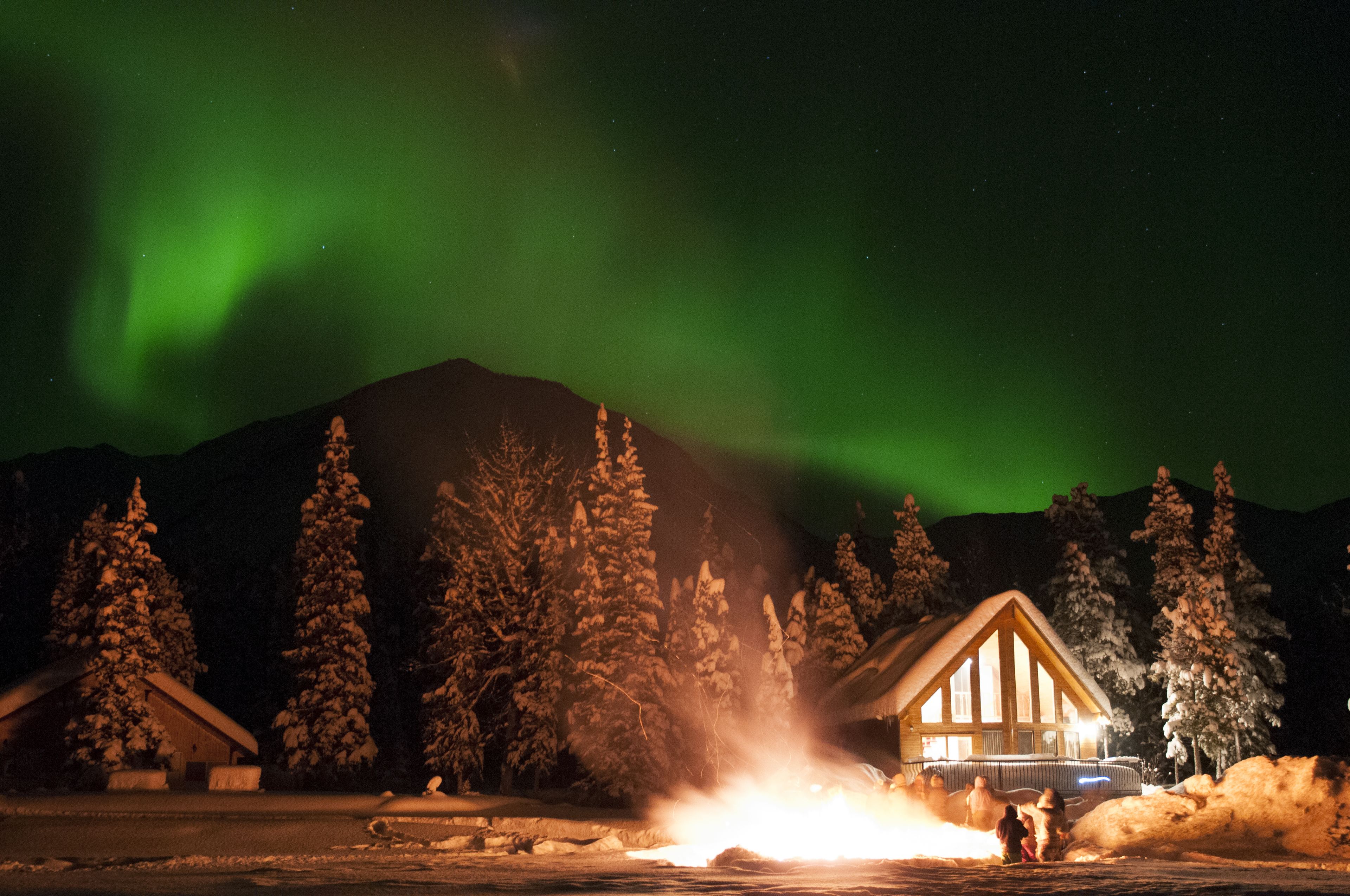 A lodge with a prominent wooden structure, surrounded by snow-covered trees and a visible fire.