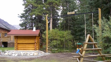 Escape to a serene cabin nestled among dense trees, with a swing set and climbing structure for outdoor fun.