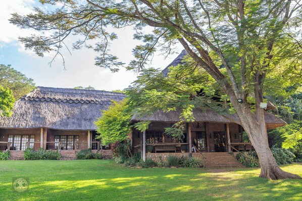 A traditional thatched-roof building with a stone foundation, surrounded by lush greenery and a well-maintained lawn. - Kumbali Country Lodge (Lilongwe)