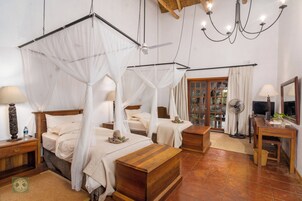 Una habitación con dos camas, un escritorio de madera, una silla, un ventilador y una ventana con cortinas.