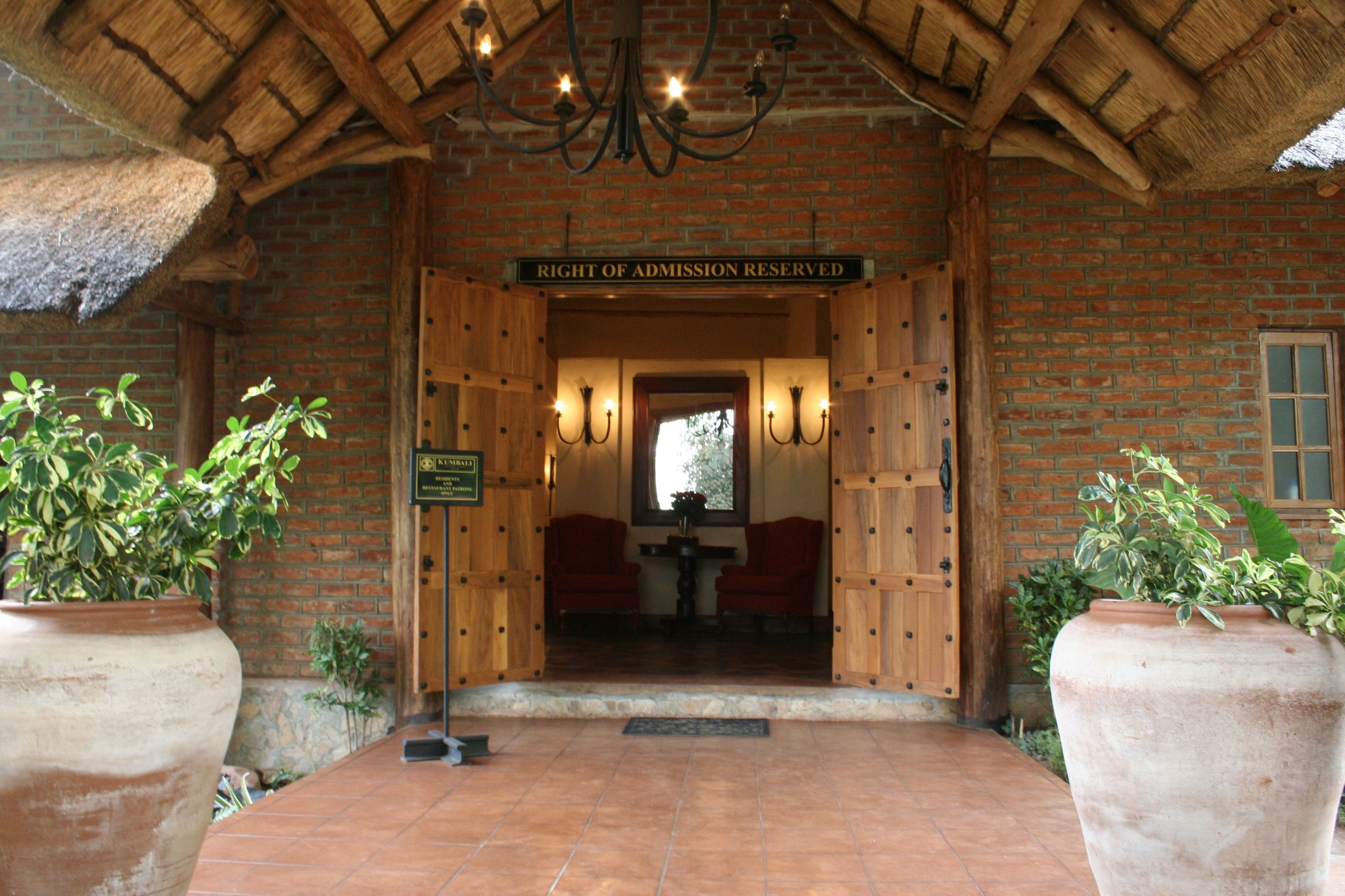 A rustic entrance with a 'Right of Admission Reserved' sign, wooden doors, and potted plants.