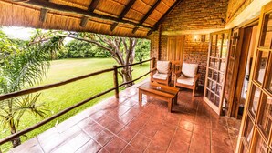 A covered patio with a wooden bench and a table, overlooking a lush garden. - Kumbali Country Lodge (Lilongwe)