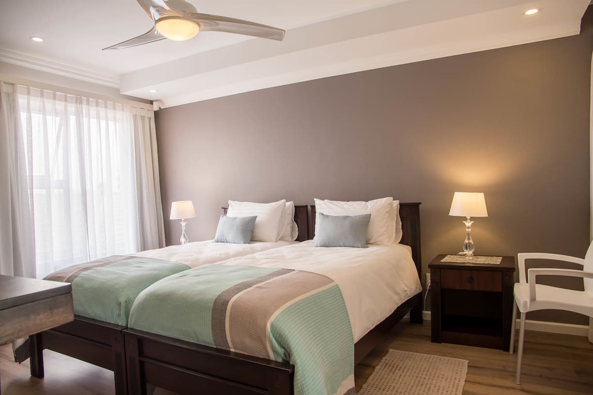 Un dormitorio con cama, mesitas de noche, una silla y un ventilador de techo.