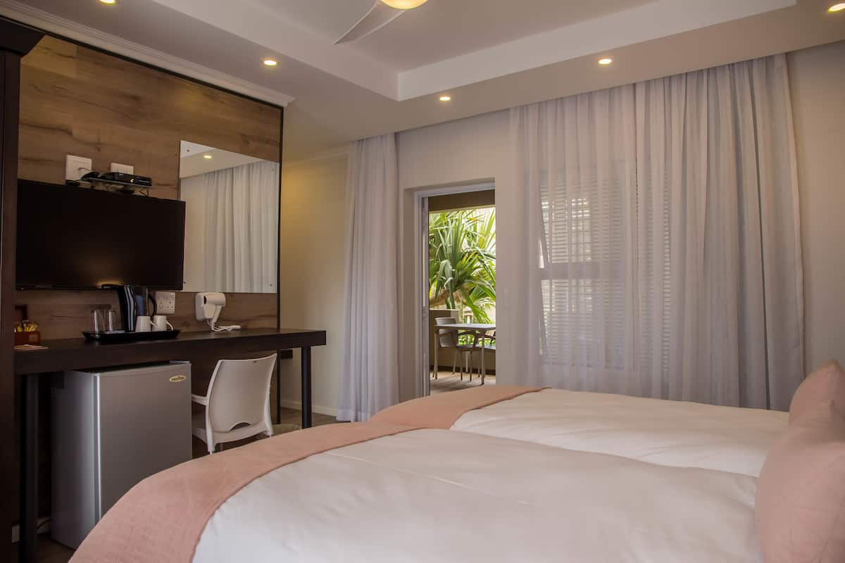Habitación de hotel con cama, escritorio con computadora, refrigerador pequeño y ventana con cortinas.