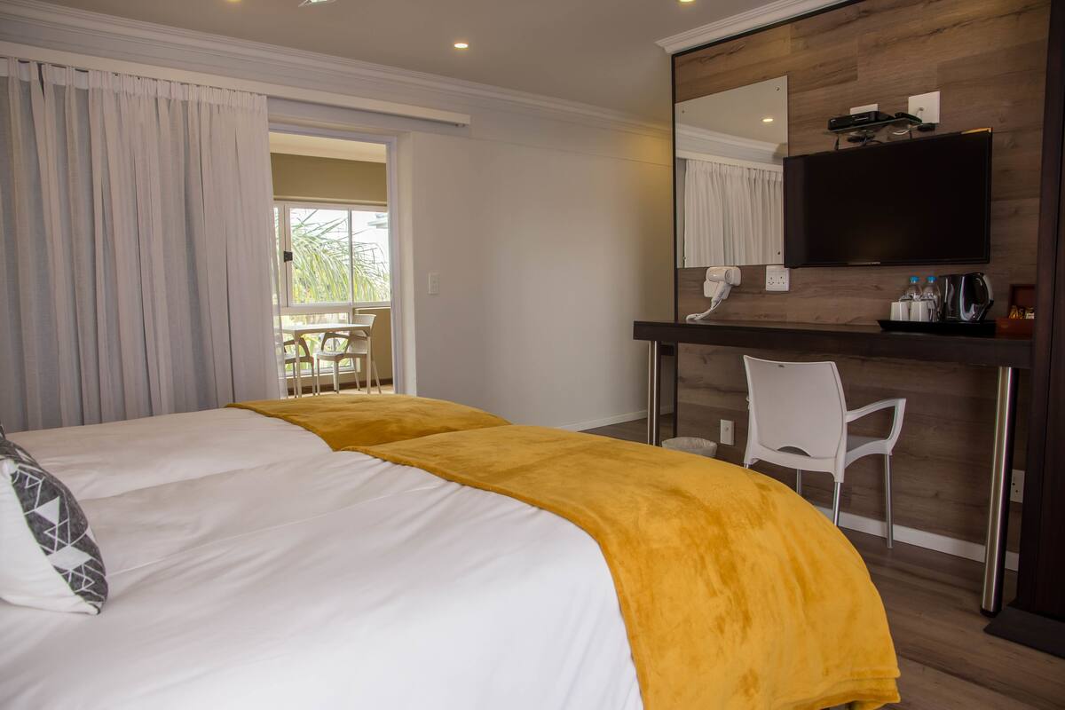 Habitación de hotel con dos camas, un escritorio con silla, un espejo grande y una televisión.