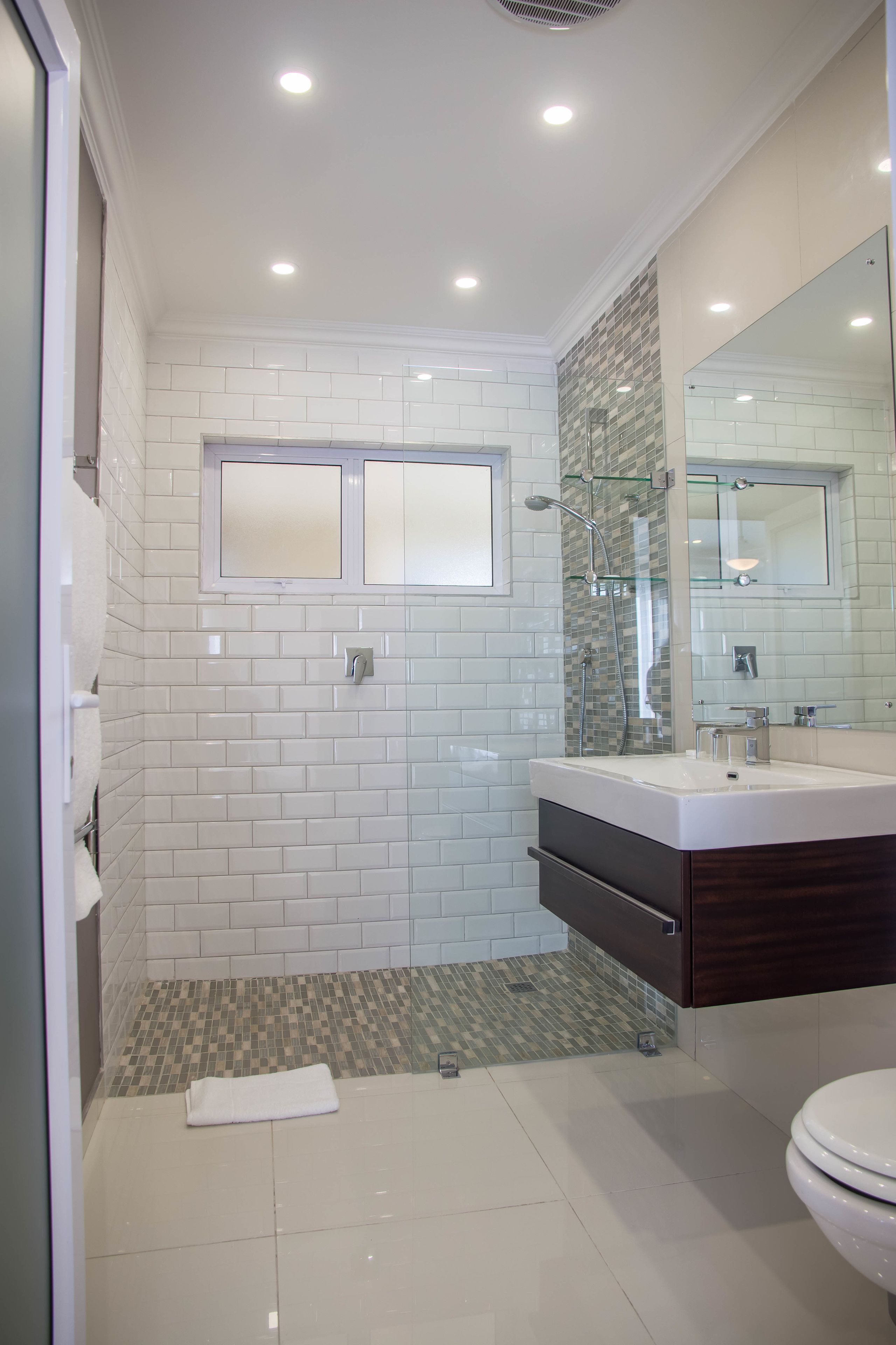 A modern bathroom with white subway tiles, a glass shower enclosure, a large mirror, and a white toilet.