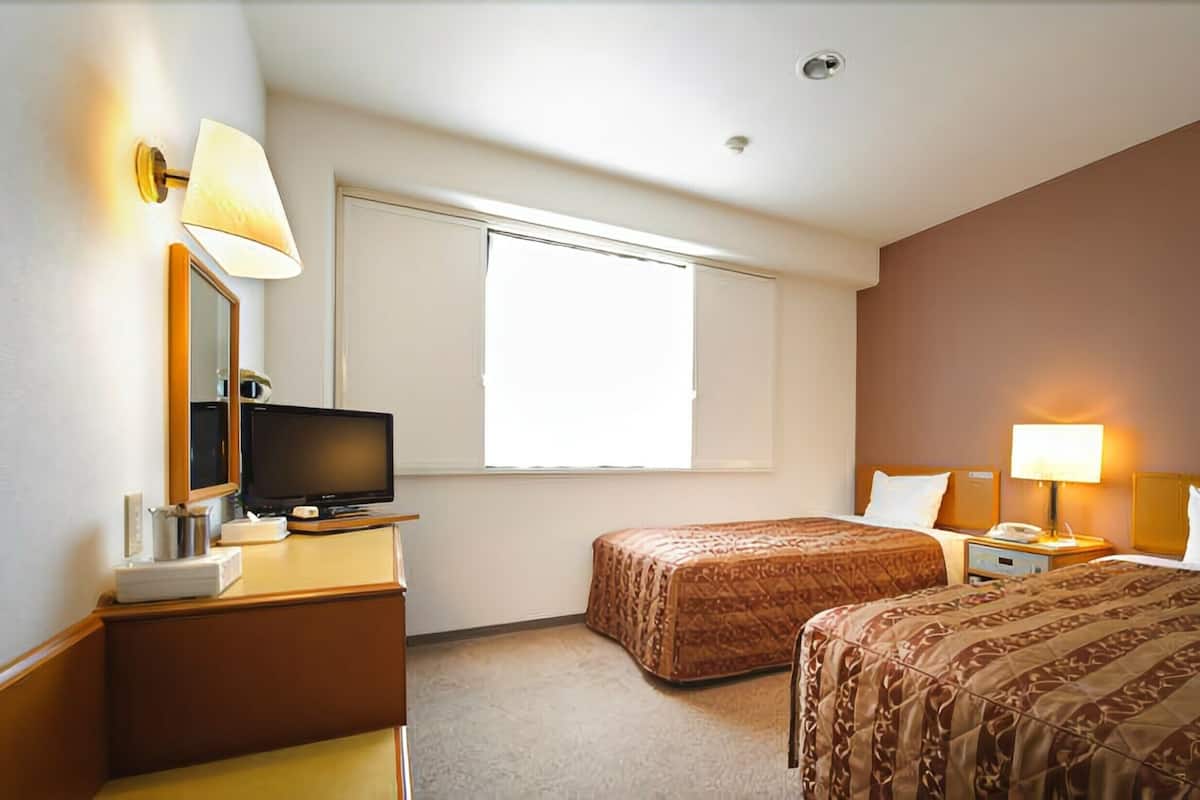 A hotel room with two beds, a television on a wooden dresser, a bedside table with a lamp, and a large window.