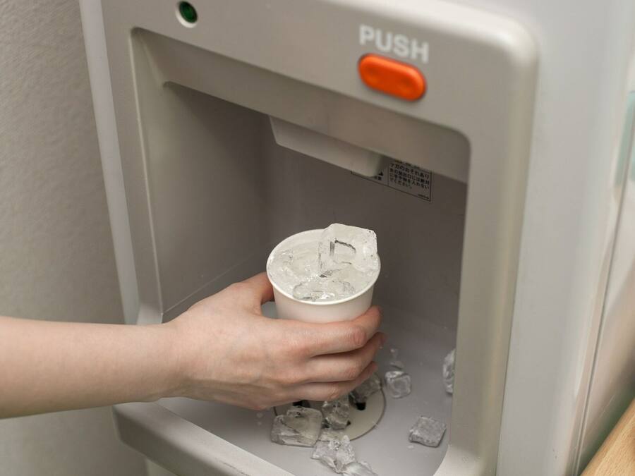A hand holding a cup with ice cubes, placed in a dispenser with a 'PUSH' button.