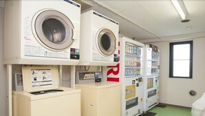 A laundry facility with multiple washing machines and dryers, a green floor, and a window with natural light. - Bells's Inn Maebashi (Maebashi)
