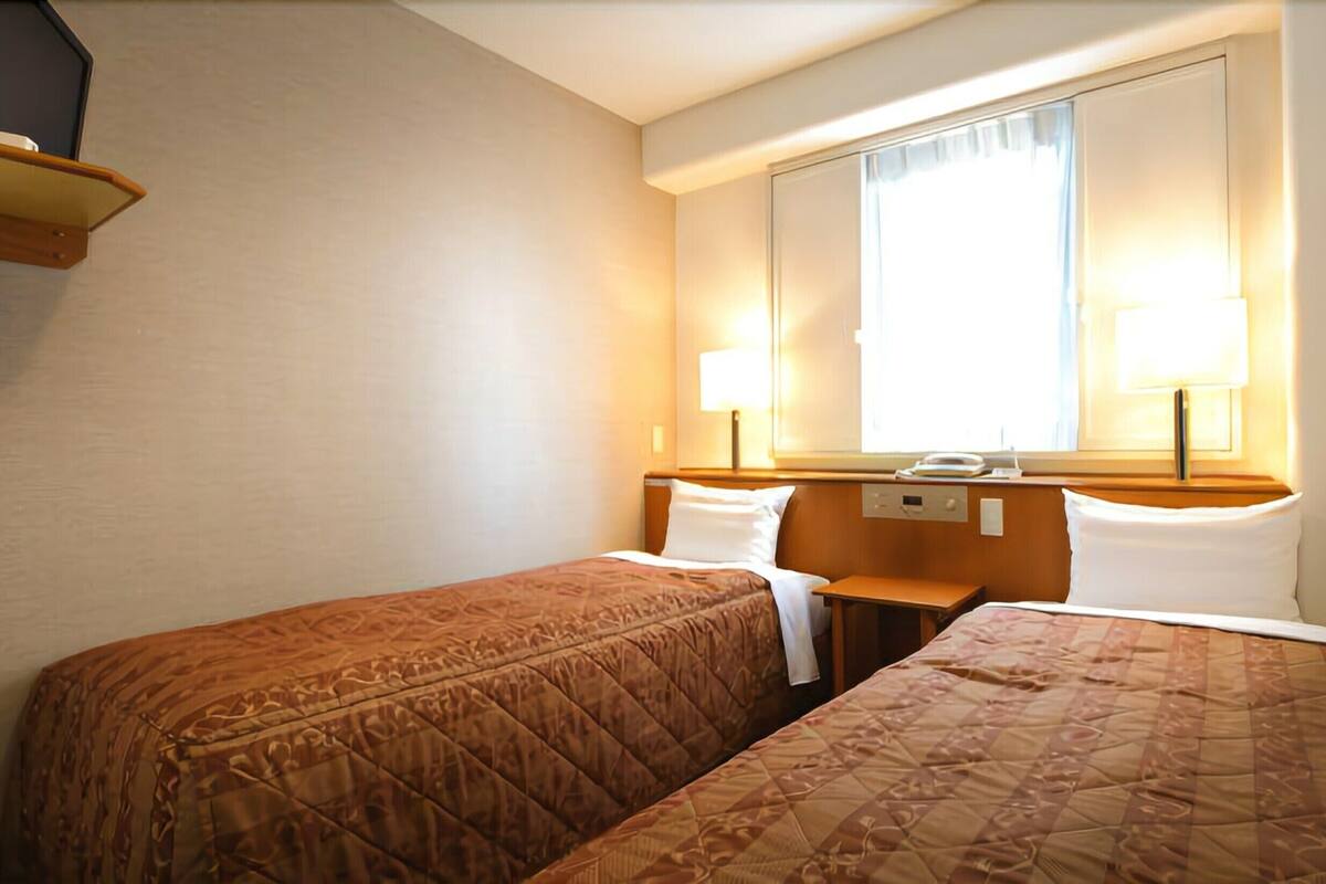 A hotel room with two single beds, a nightstand, a mirror, and a window with curtains.