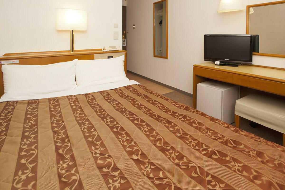 A hotel room with a bed, a desk with a television, and a mirror.