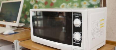A white microwave oven on a wooden shelf with a floral wallpaper background.