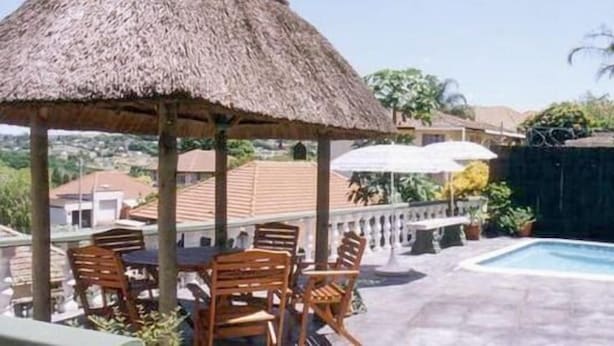 A poolside area with a thatched umbrella, wooden chairs, and a pool. - The Troll and Tulip (Durban)