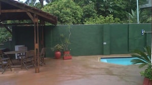An outdoor patio with a pool, wooden furniture, and a green wall. - The Troll and Tulip (Durban)