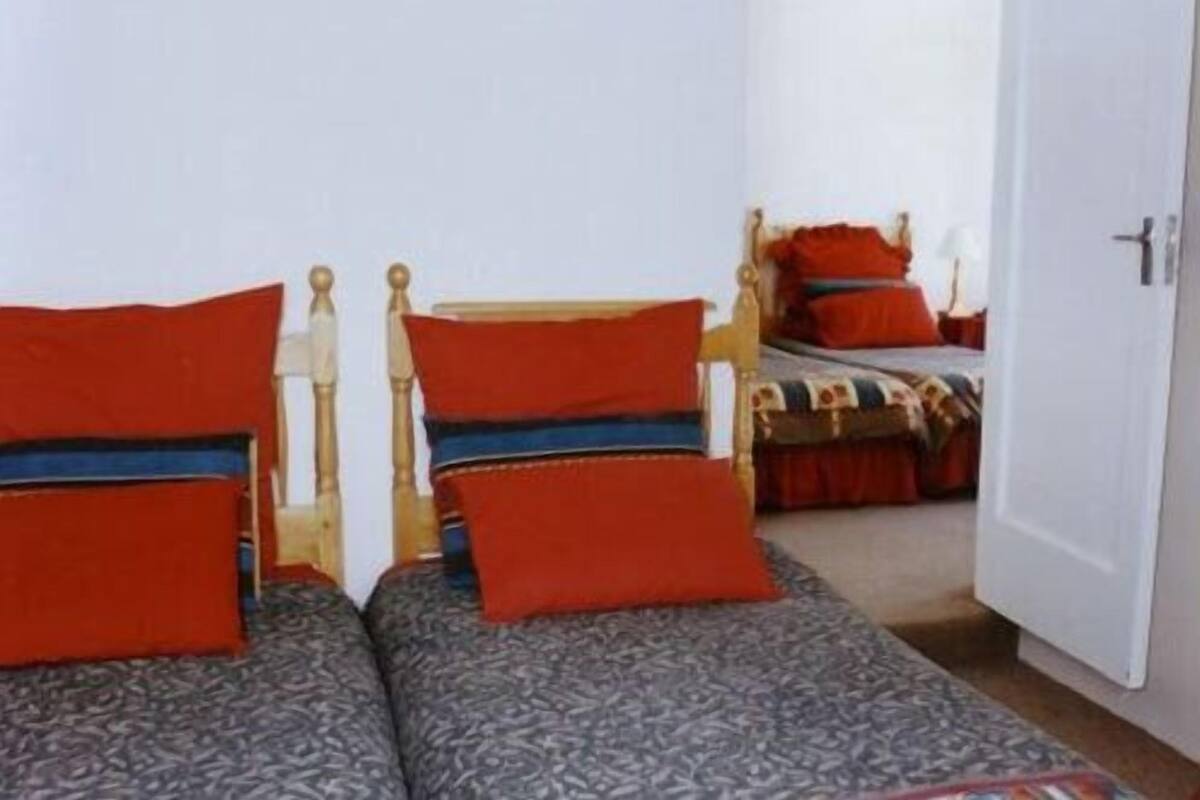 A room with two single beds with wooden frames and red and blue bedding.