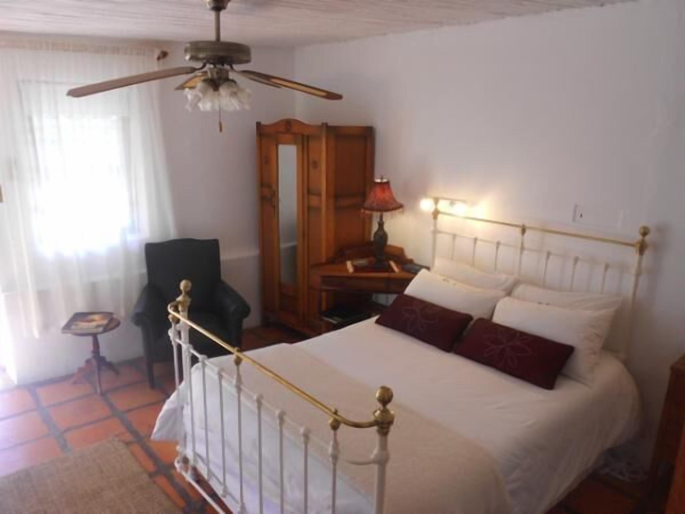 Un dormitorio con cama, una silla, un escritorio, una lámpara y un ventilador de techo.