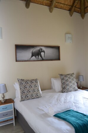 Un dormitorio con cama, almohadas estampadas, un cuadro de un elefante, una mesita de noche y una lámpara.