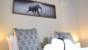 A hotel room with a thatched roof, a bed with patterned pillows, and a framed picture of an elephant on the wall. - Raptors Wildlife Escapes (Hoedspruit)