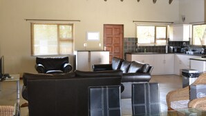 A spacious living area with a high ceiling, a dining table with chairs, a sofa, and a kitchen in the background. - Raptors Wildlife Escapes (Hoedspruit)