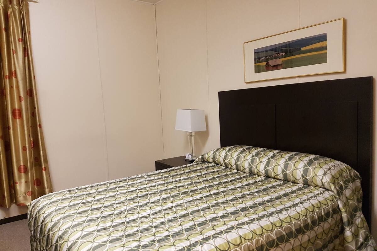 Una habitación de hotel con una cama, una mesita de noche, una lámpara, una cortina y un cuadro en la pared.