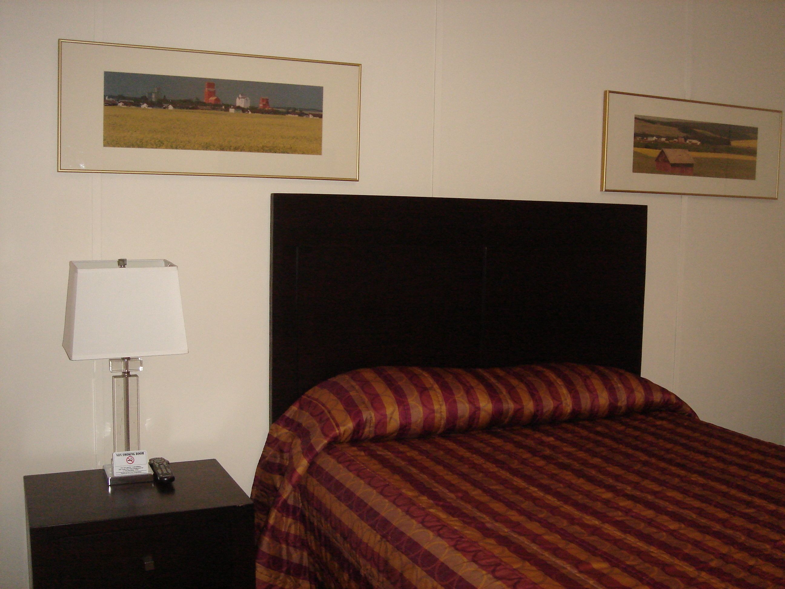 A hotel room with a bed, a nightstand with a lamp, and two framed pictures on the wall.