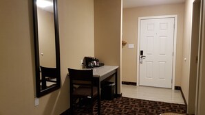 Hotelkamer met een bureau, stoel en een grote spiegel. Er is een deur met een hendel en een lichtschakelaar aan de muur.