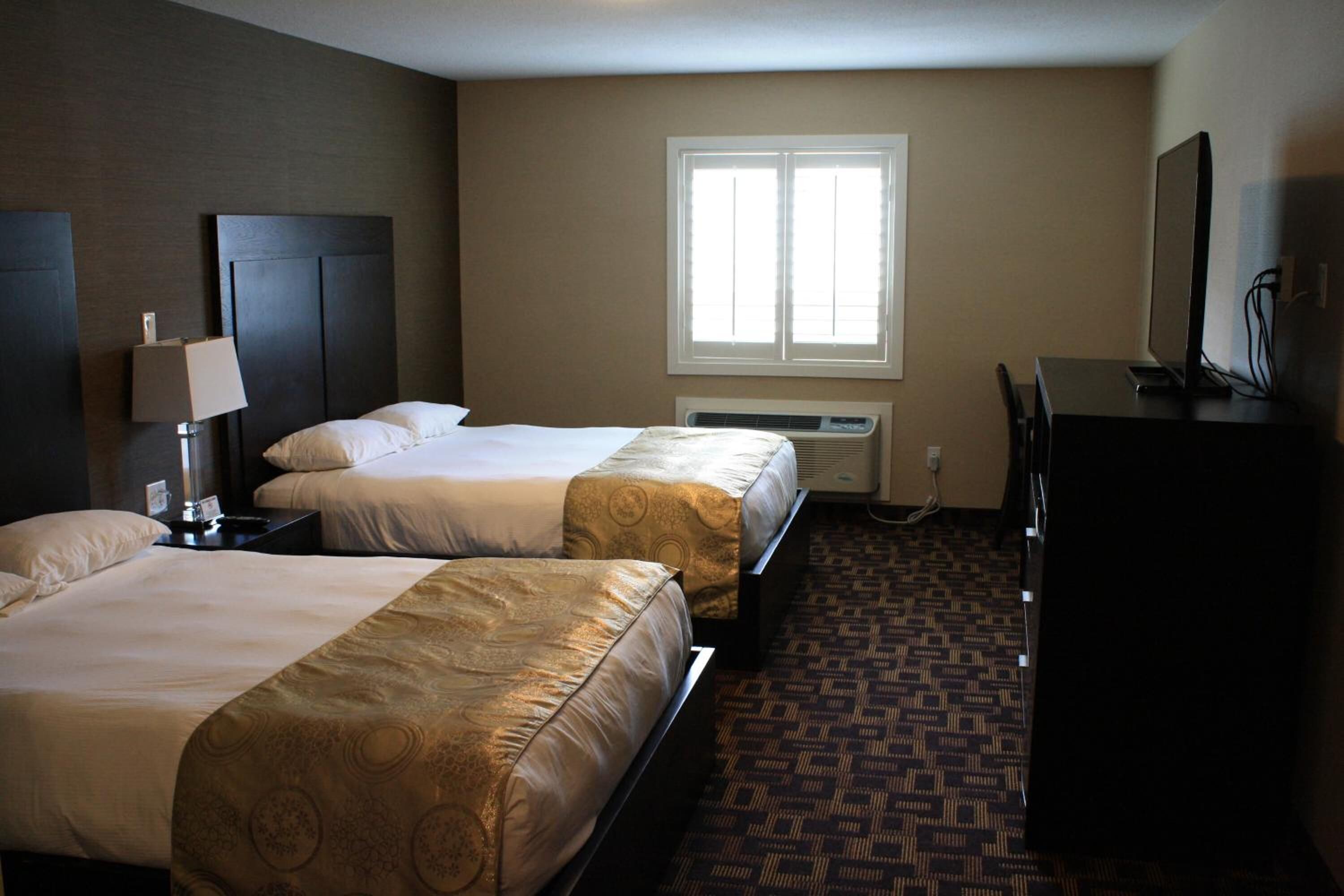 A hotel room with two beds, a desk, a lamp, a TV, and a window.