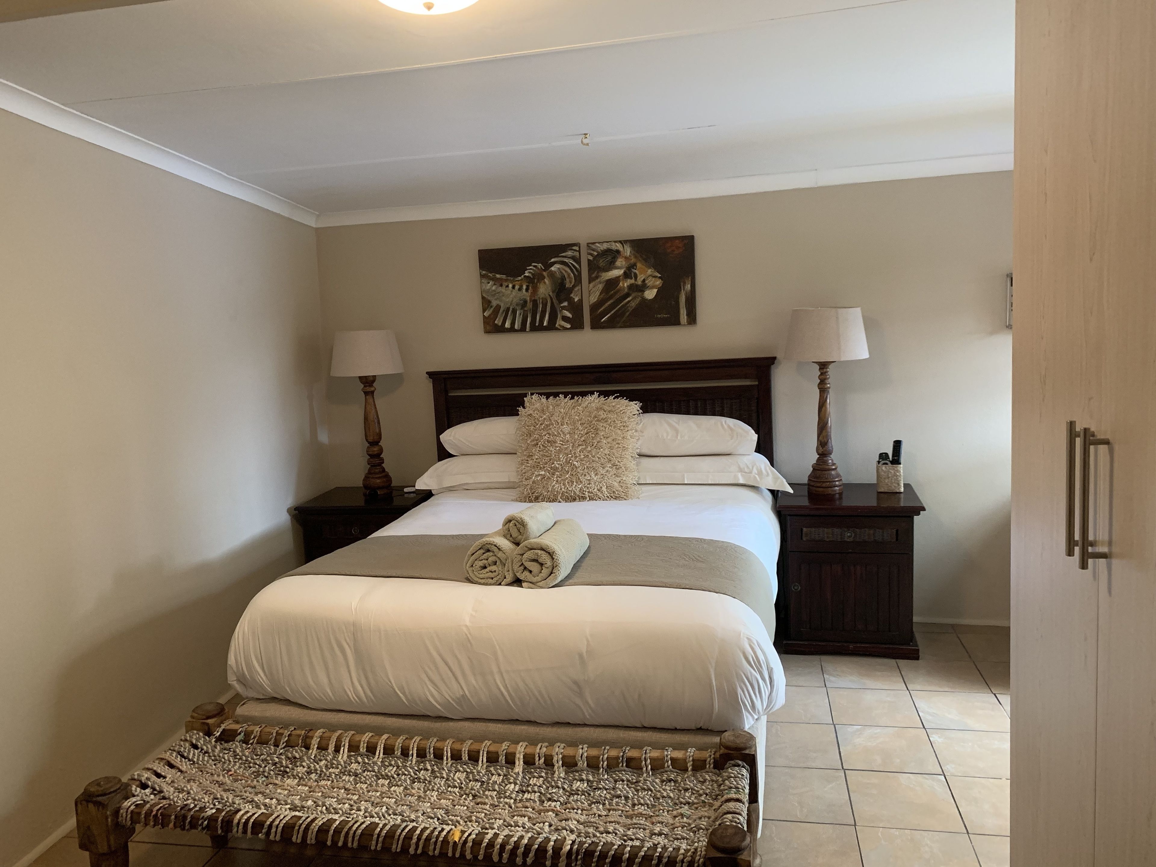 A neatly arranged bedroom with a large bed, two bedside tables with lamps, a bench, and a wall-mounted shelf.