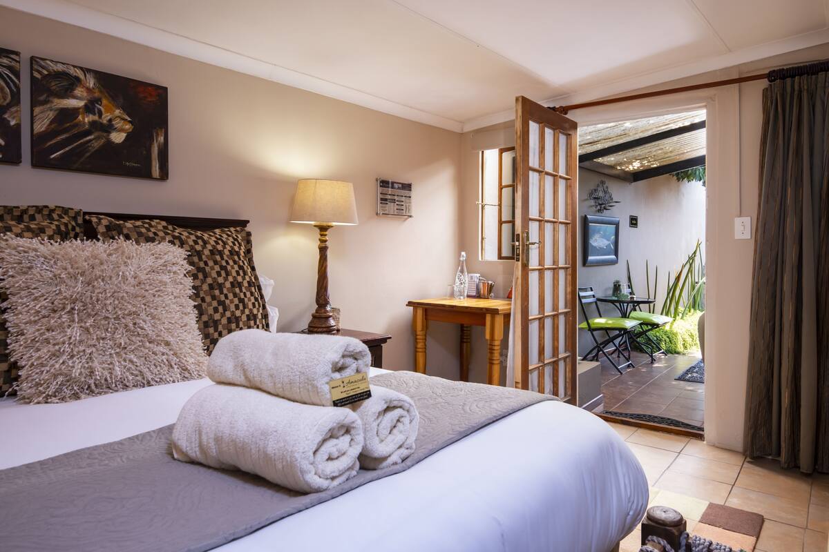 A hotel room with a bed, a lamp, a small table, and a view of the outdoor patio.