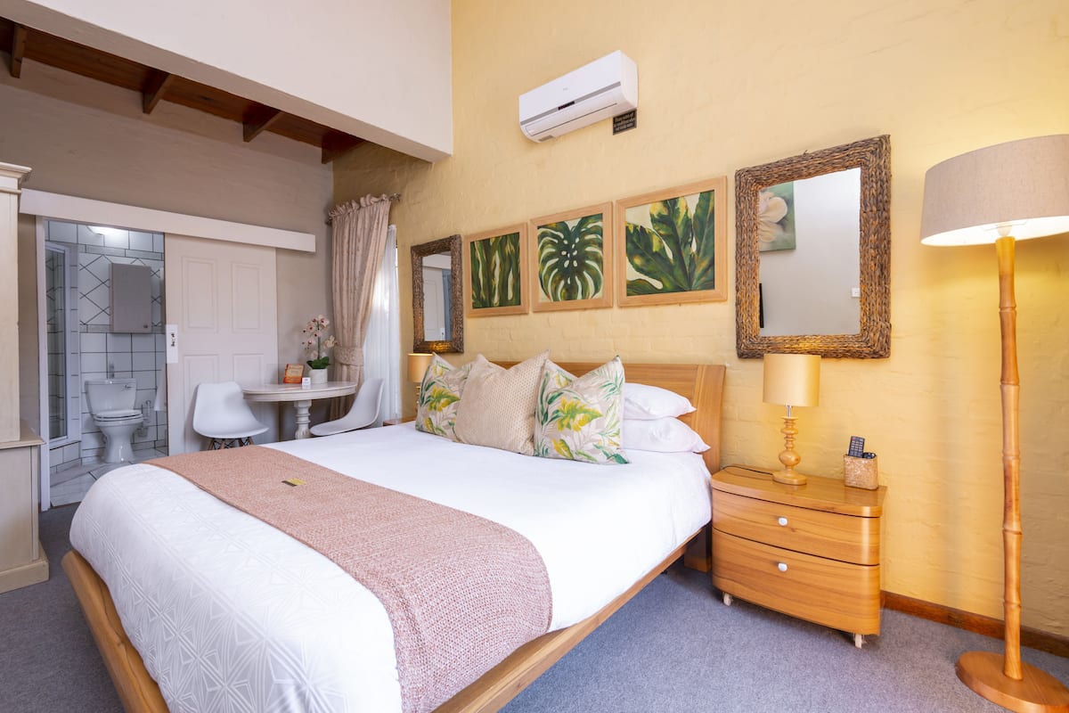 A bedroom with a large bed, bedside table, and a mirror. There is a bathroom with a toilet and sink.