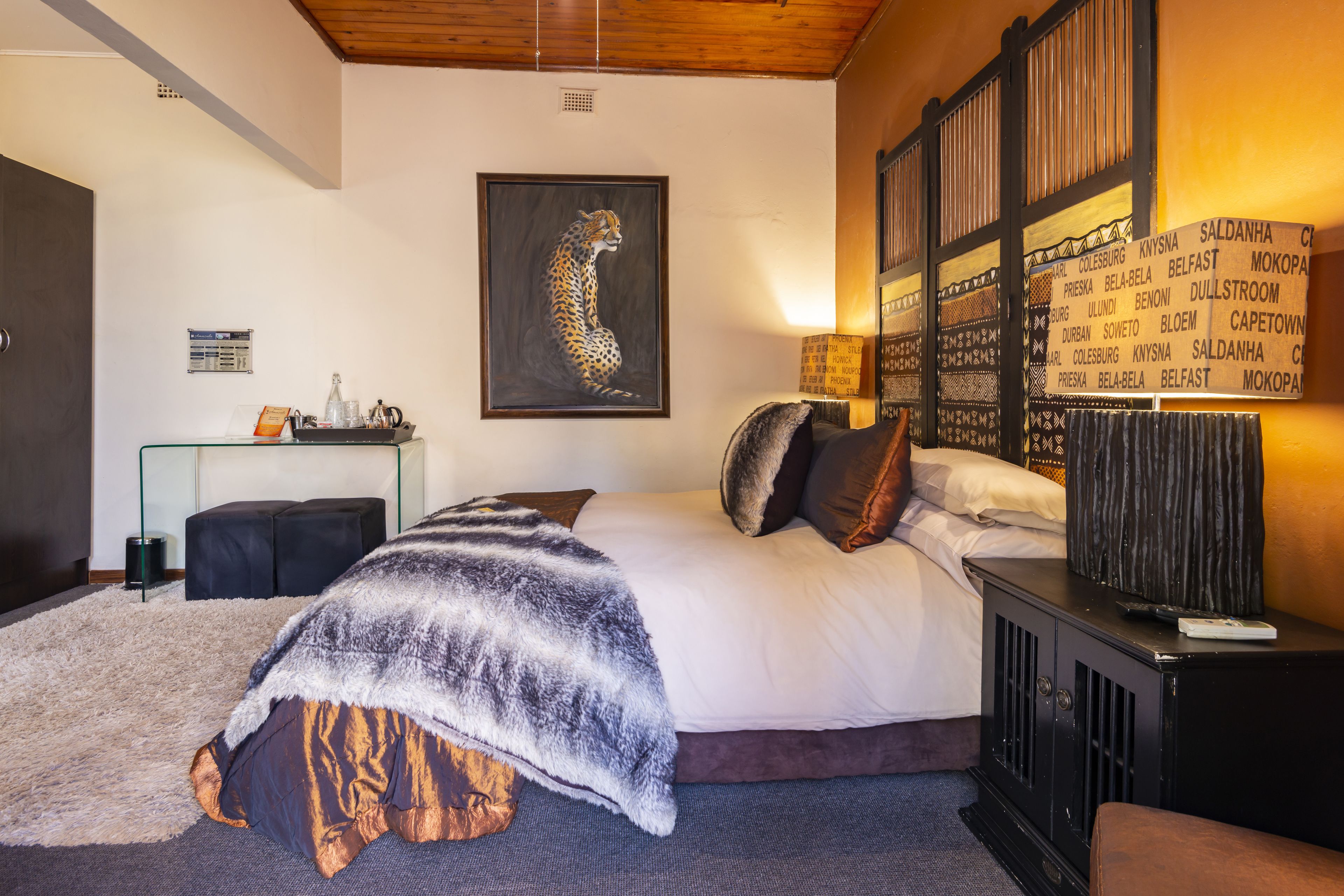 A bedroom with a large bed, a leopard painting, a wooden headboard, and a wall with a list of city names.
