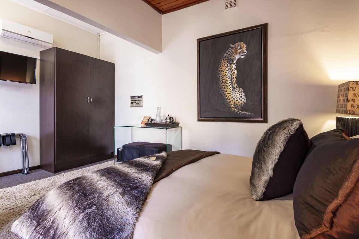 A bedroom with a large bed, a wardrobe, a glass table with a lamp, and a leopard painting on the wall.
