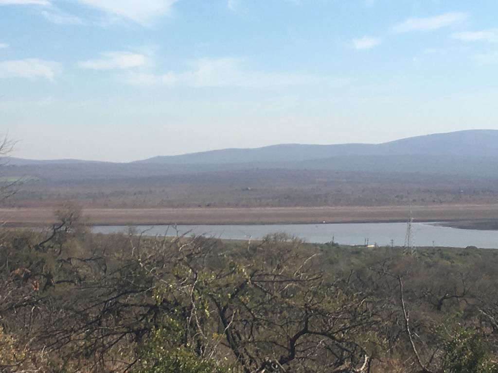 A landscape with a body of water, distant hills, and sparse vegetation.