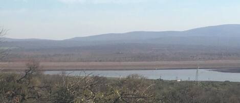 A landscape with a body of water, distant hills, and sparse vegetation.