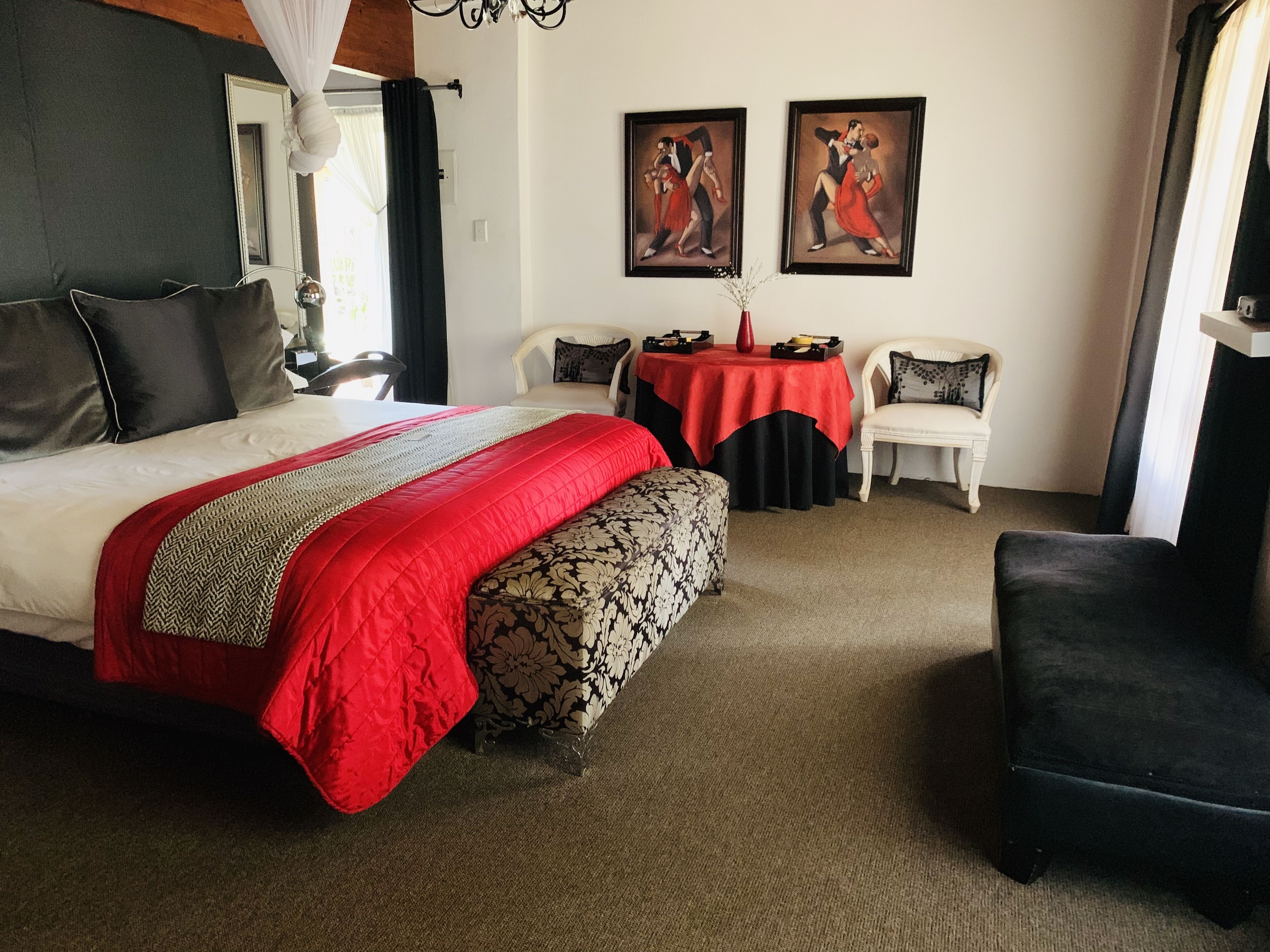 A hotel room with a large bed, a small table, two chairs, and two paintings on the wall.