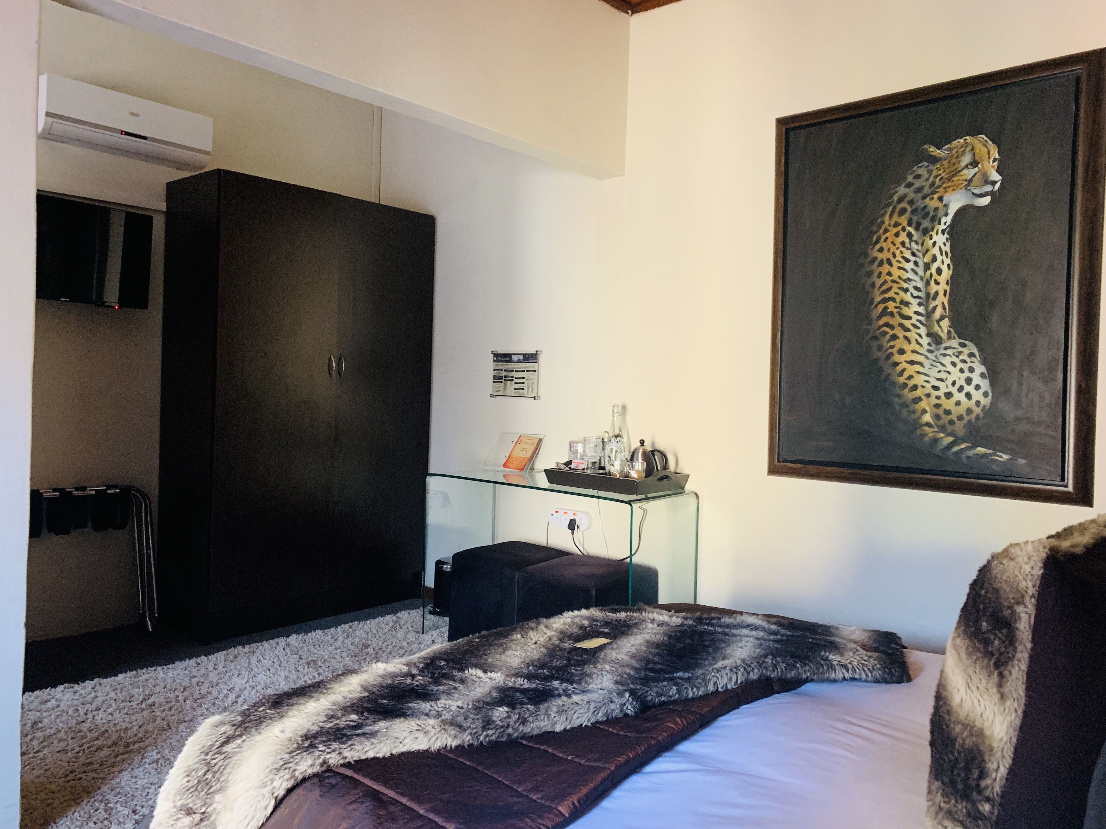 Ein Hotelzimmer mit einem Bett, einem Glastisch mit einer Gepard-Zeichnung, einem dunklen Schrank und einem Kleiderständer.