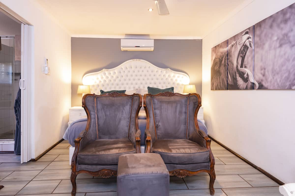 A bedroom with a large bed, two upholstered chairs, a small table, and a wall-mounted air conditioner.