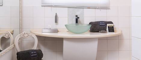 Une salle de bain avec un meuble-lavabo blanc, un lavabo en forme de bol en verre, un porte-serviettes et un miroir.