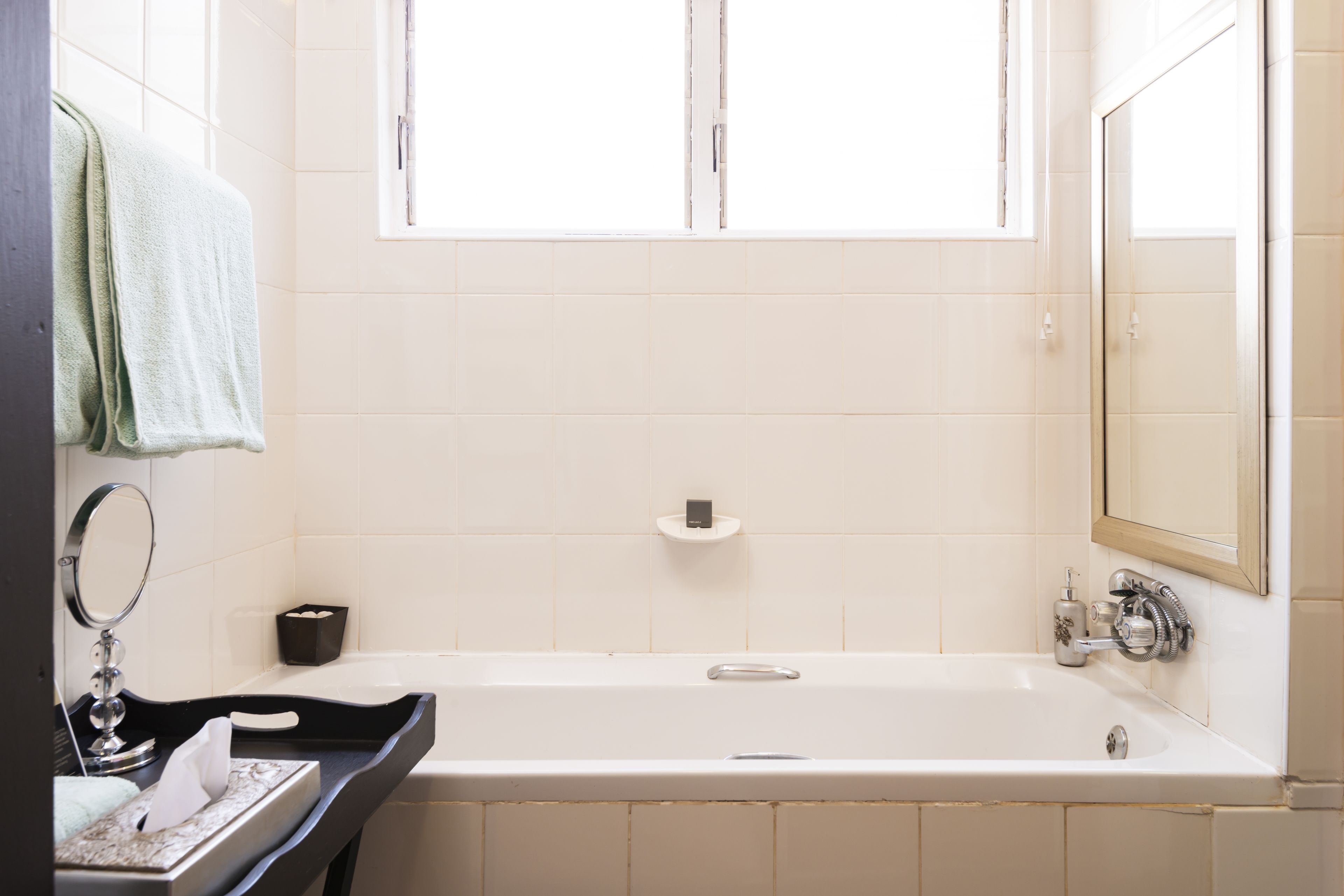 Ein Badezimmer mit einer Badewanne, einem Spiegel, einem Handtuchhalter und einem Fenster.