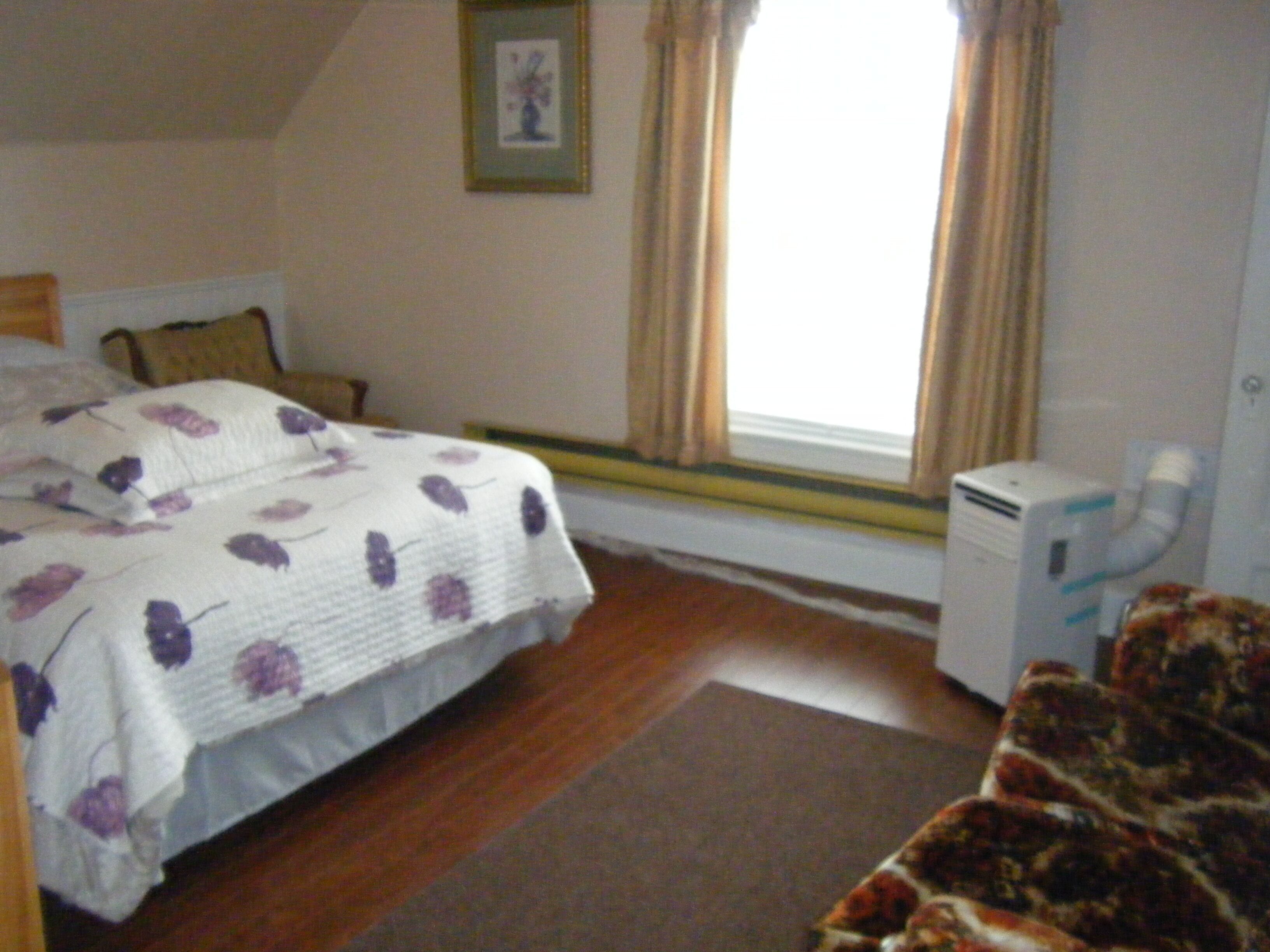 Une chambre à coucher avec un lit, une table de chevet, un radiateur et une fenêtre avec des rideaux.