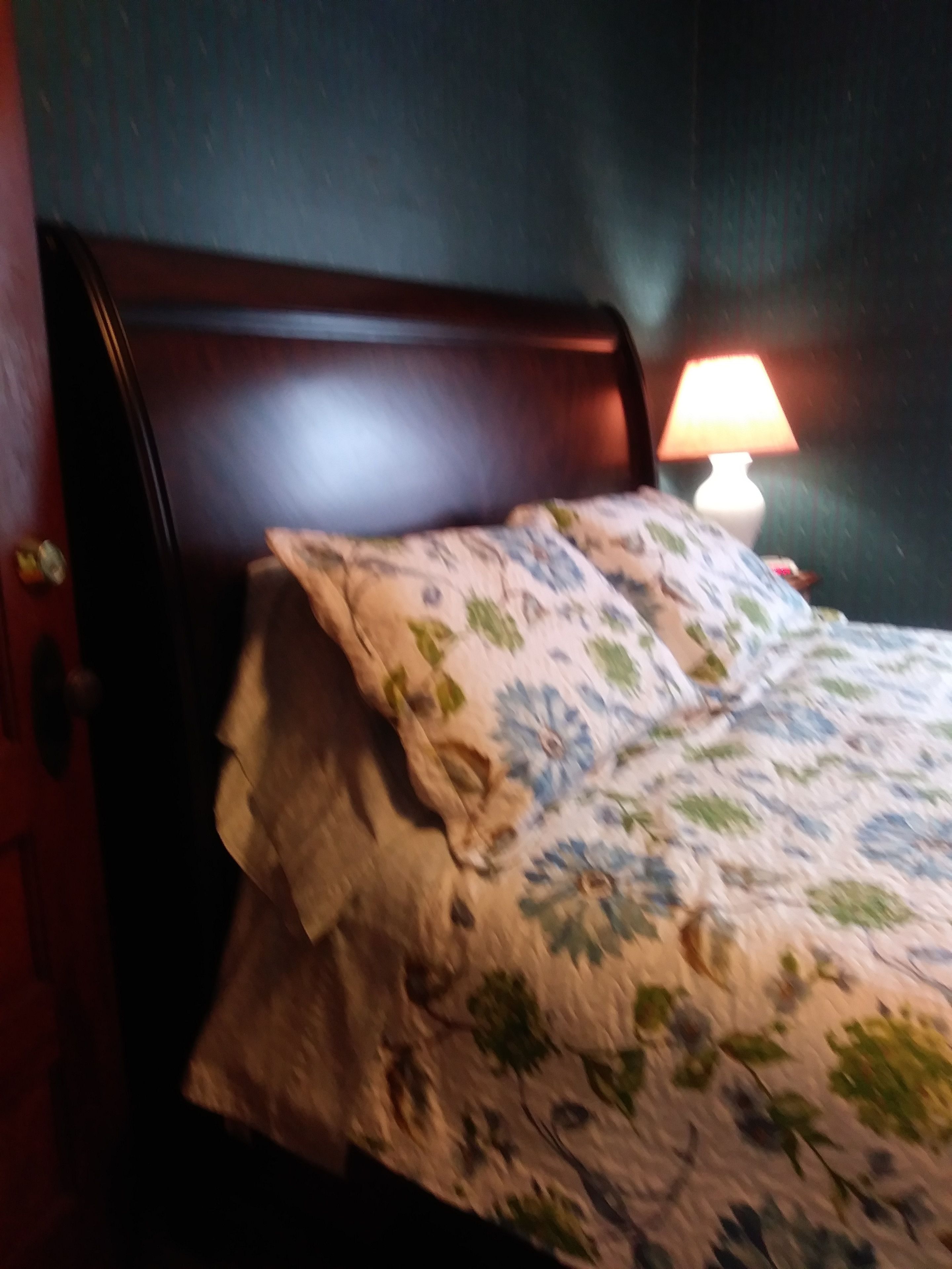 Un lit avec une couvre-lit à motifs floraux, une tête de lit en bois et une lampe de chevet.