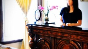 A wooden reception desk with a vase of pink flowers and a clock.
