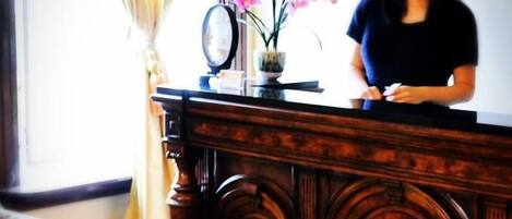 A wooden reception desk with a vase of pink flowers and a clock.