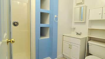 Un baño con ducha, inodoro, lavabo y estantes empotrados.