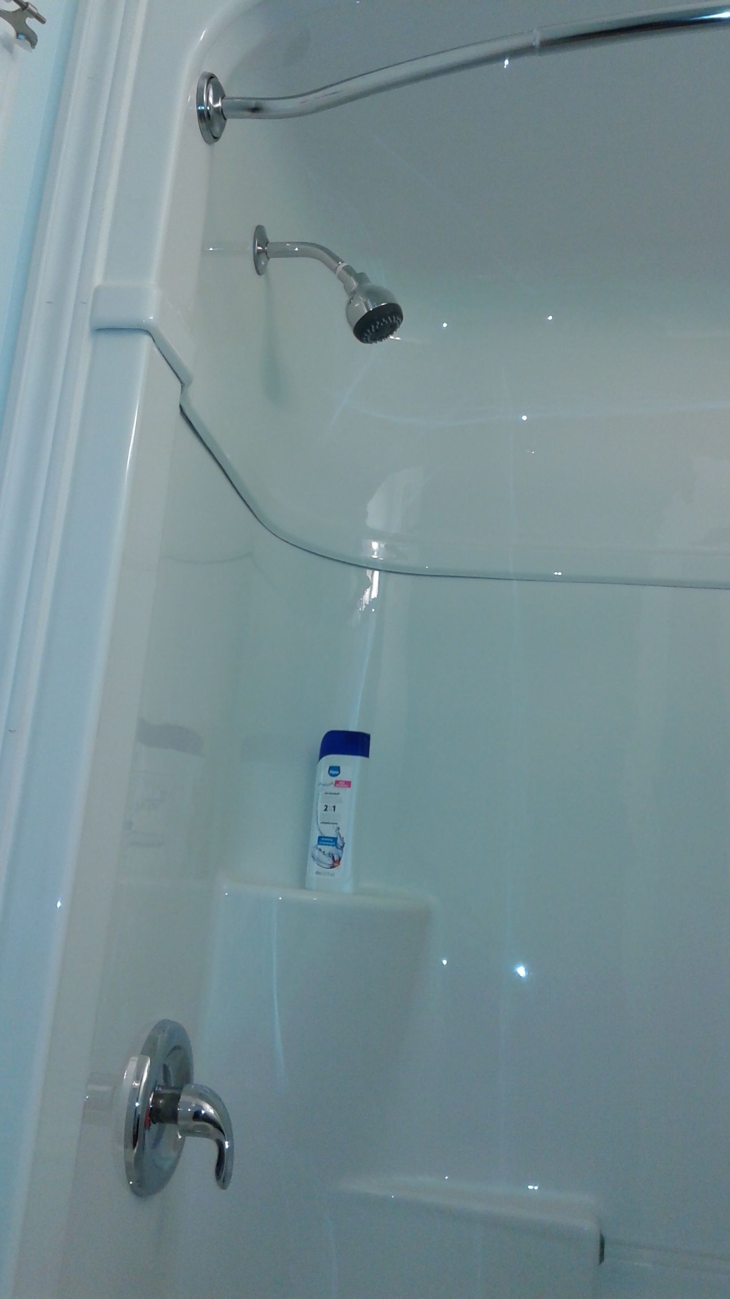 Une baignoire blanche avec un pommeau de douche amovible et une bouteille de shampoing.