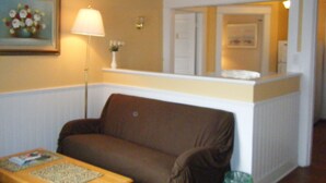 A living room with a brown sofa, a small table with a lamp, and a framed picture on the wall.