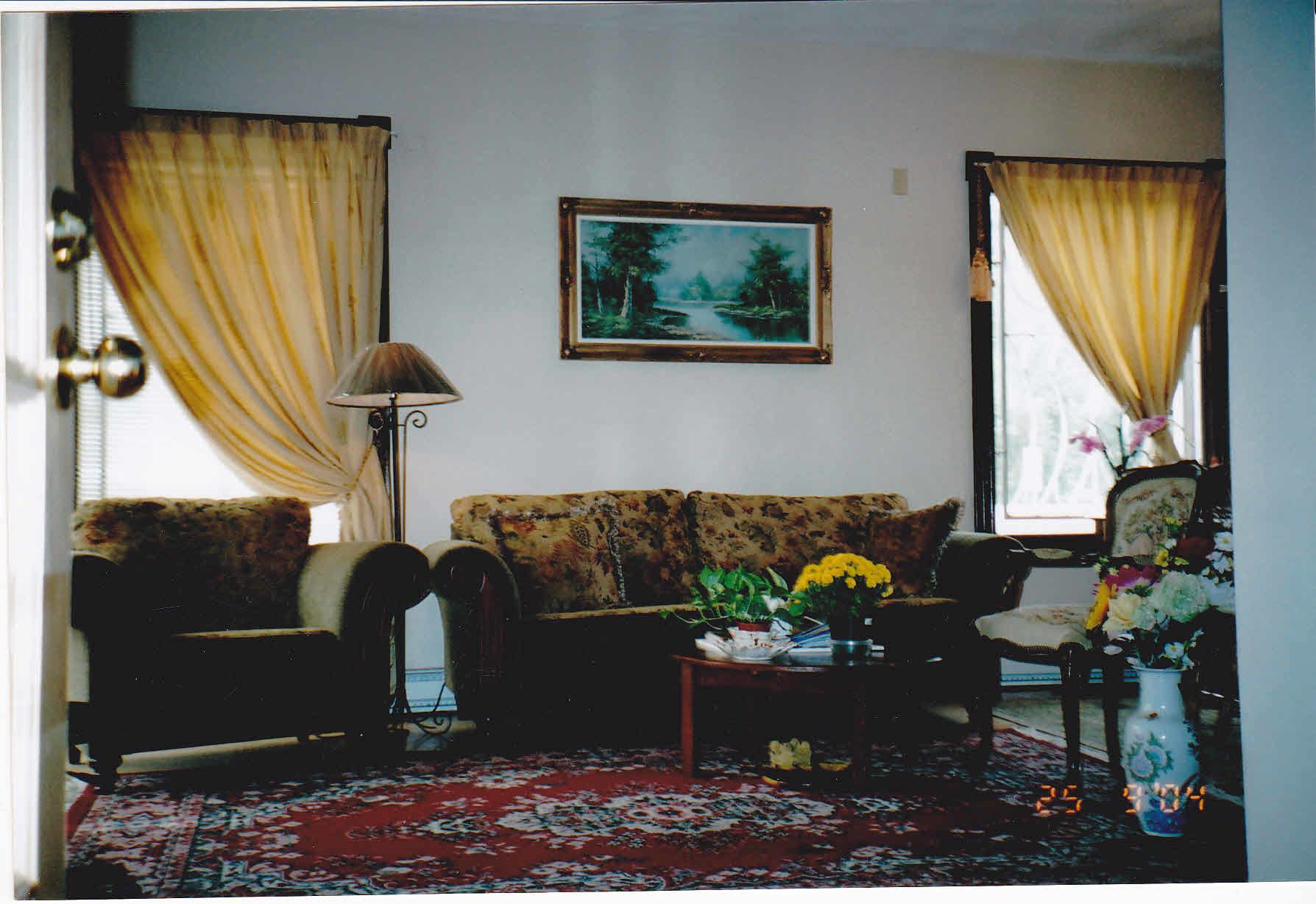 A living room with a sofa, armchairs, a coffee table with flowers, a lamp, and a painting on the wall.