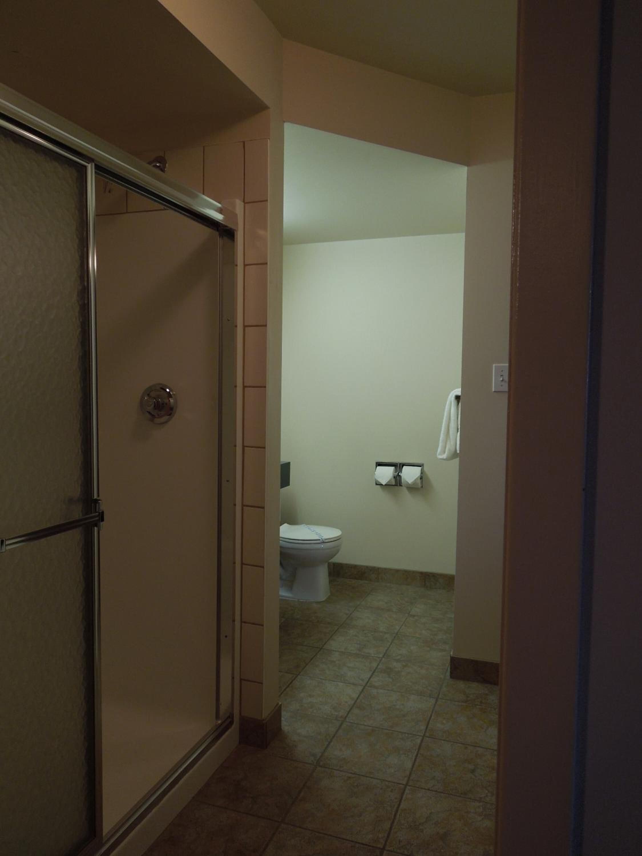 Un couloir menant à une salle de bain équipée de toilettes, d’un porte-serviettes et d’un espace douche.