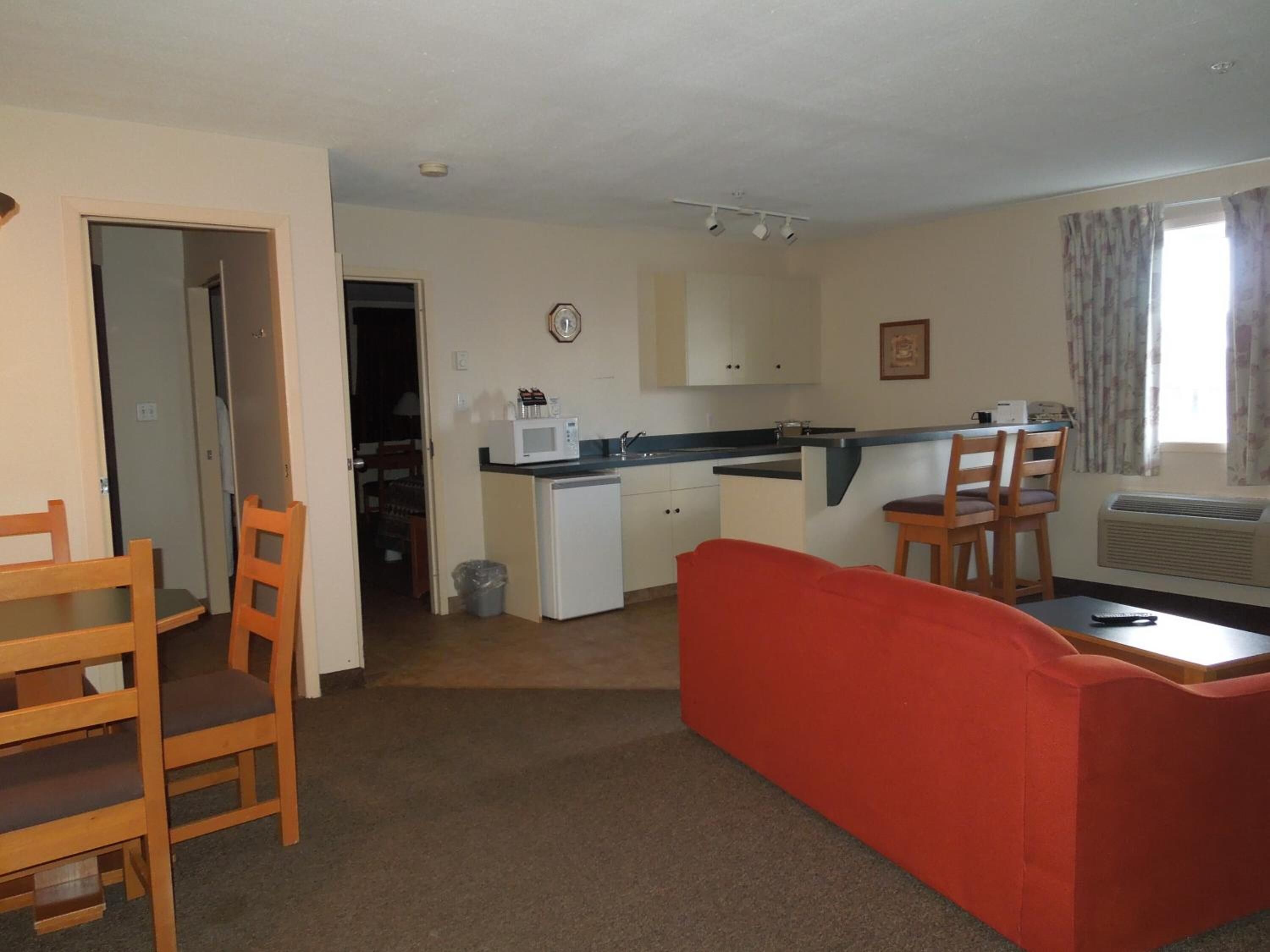 A compact living space with a kitchenette, a dining area with wooden chairs, and a red sofa.
